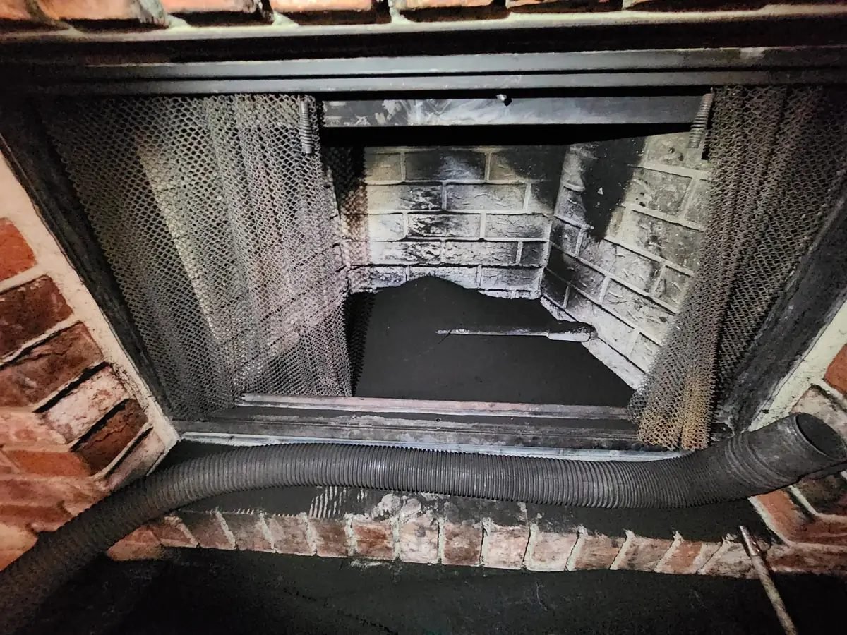 Soot-blackened firebox interior with the fire screen folded back and a sweep hose fed up past the damper